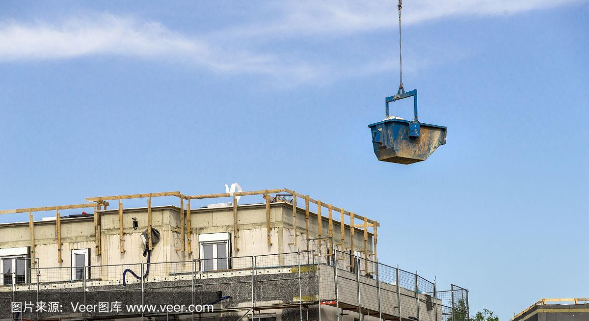 一个装有建筑材料的蓝色容器漂浮在建筑工地的上方,与大型办公楼的